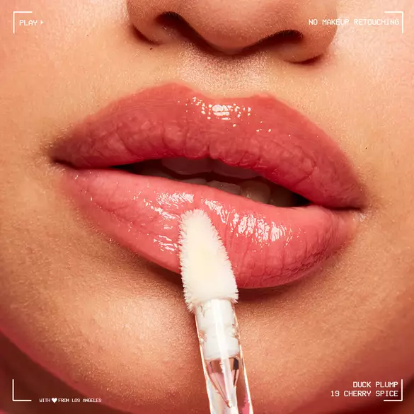 Glossy lippen met een applicator, in de context van een cosmetisch product \'Duck Plump 19 Cherry Spice\'.
